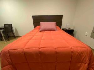 Una cama grande de color naranja con una almohada rosa. en Smart studio en Cochabamba