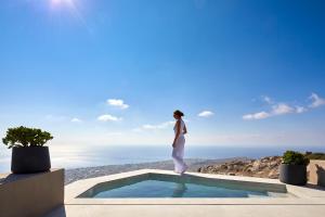 a woman standing on the edge of a pool overlooking the ocean at Santorini Sky, The Lodge in Pyrgos