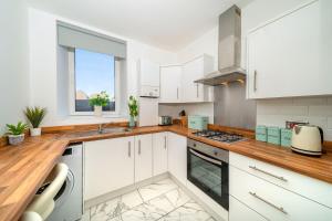 cocina con armarios blancos y encimera de madera en Cleppie Apartment en Dundee