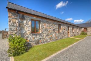 a stone building with a grass yard in front of it at Carnedd Cottage in Dwyran