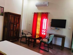 a room with a bed and a tv and chairs at Rose Cottage - A Heritage Retreat in Mount Ābu