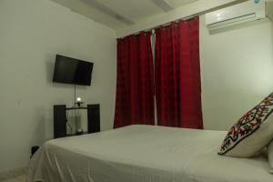 1 dormitorio con 1 cama con cortinas rojas y TV en Casa Bautista Apartamentos Amoblados con vista al mar, en Taganga