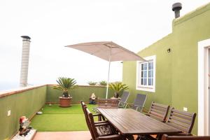 eine Terrasse mit einem Holztisch, Stühlen und einem Sonnenschirm in der Unterkunft Green Sky in San Juan de la Rambla