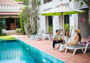 a group of people sitting under an umbrella by a pool at Monaburi Boutique Resort in Rawai Beach