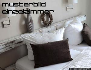 ein Bett mit weißen Kissen und einem Kopfteil aus Holz in der Unterkunft Sandbank Hotel & Appartements Lubmin in Lubmin