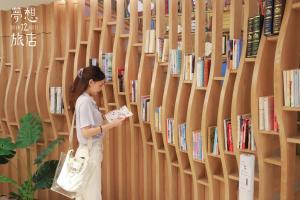 Una donna in piedi in una biblioteca che guarda un libro di Dream 12 Hotel a Taichung