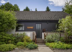 una pequeña casa gris con puerta y escaleras en Croftwood Cottage, en Boat of Garten