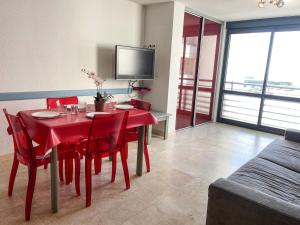 a red dining room table with red chairs and a tv at Apartment Les Rivages de Rochelongue-3 by Interhome in Cap d'Agde
