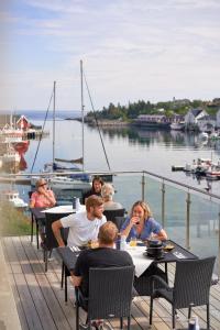 a group of people sitting at tables on a deck near a boat at The Tide - Hotel in Sørvågen