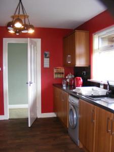 a kitchen with red walls and a washing machine at Dingieshowe Cottage in Lennoxtown