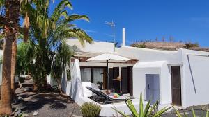 a white house with chairs and an umbrella and palm trees at Casa EL JARDIN in Morro del Jable