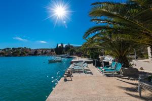 um grupo de cadeiras e palmeiras ao lado de uma massa de água em Adria House Dubrovnik by the sea em Zaton