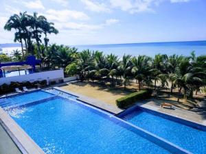 a large swimming pool with palm trees and the ocean at Resort Playa Azul 3 Dormitorios in Tonsupa