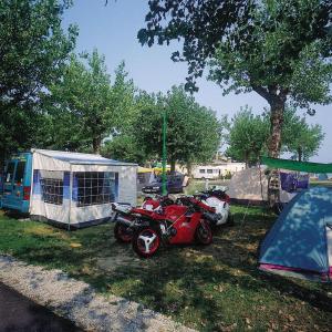 a red motorcycle parked in the grass next to a tent at Camping Wien in Peschiera del Garda