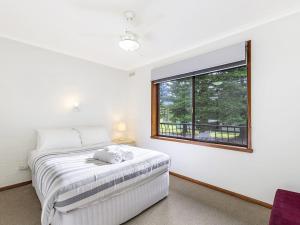 a white bedroom with a bed and a window at Eastern Beach Unit 6 in Port Fairy