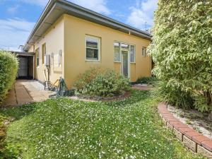 a yellow house with a yard with white flowers at Fairholme Apartment in Warrnambool