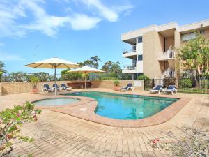 a swimming pool with chairs and an umbrella and a building at Headlands 10 Two Bedroom Beachside Apartment with Magical Ocean Views Great Value for Money in Alexandra Headland