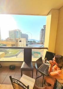uma mulher sentada numa mesa com um laptop na frente de uma janela em DXB Backpackers em Dubai
