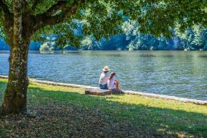 a man and a child sitting next to a lake at Camping Le château du gibanel in Saint-Martial-Entraygues +49 photos