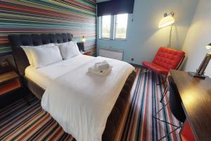 a hotel room with a large bed and a red chair at Village Hotel Birmingham Walsall in Walsall