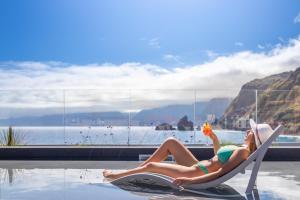 a woman sitting in a chair next to a swimming pool at Aqua Natura Bay in Porto Moniz