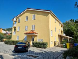 a yellow building with a car parked in front of it at Apartments Gorica 1 in Baška