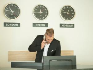 a man talking on a cell phone at a desk with clocks at Stadthotel Donauwörth in Donauwörth