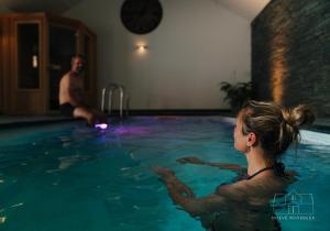 a woman in a swimming pool with a man in the background at Hoeve Roosbeek in Zepperen