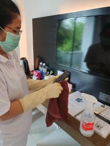 a woman wearing a mask and gloves holding a remote control at Hotel Chuan Chom The High Resort Saraburi - SHA Plus in Sara Buri