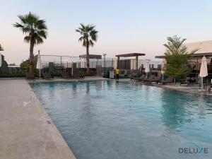 a large swimming pool with palm trees on a building at Extensive 3BR Townhouse at Janusia Damac Hills 2 by Deluxe Holiday Homes in Dubai