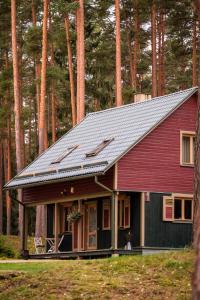 a red house with a gray roof in front of trees at LVM tūrisma un atpūtas centrs "Spāre" in Spāre