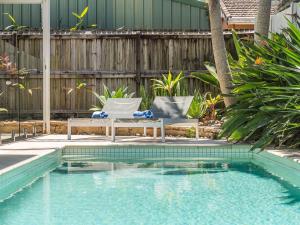 a swimming pool with two lounge chairs next to a fence at Elua Beach House in Byron Bay