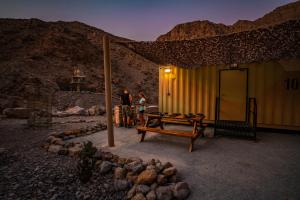 twee mensen staan buiten een geel gebouw met een tafel bij Bear Grylls Explorers Camp in Ras al Khaimah