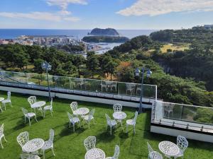 un balcón con sillas blancas y mesas en el césped en Casaloma Hotel, en Seogwipo