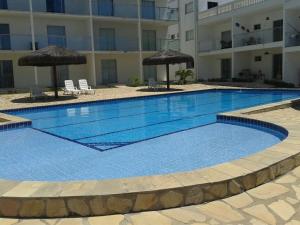 a large swimming pool with two umbrellas and a building at Apartamento VISTA MAR - Condomínio Granito e Jasmim in Jacumã