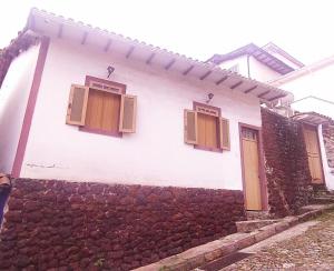 a white house with two windows and a stone wall at Oro Hospedaria in Ouro Preto