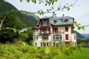 een groot huis in een veld met bergen op de achtergrond bij La Grande Savoyarde in Chamonix-Mont-Blanc
