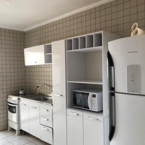 cocina blanca con nevera y microondas en apartamento bombinhas, en Bombinhas