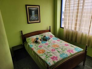 un pequeño dormitorio verde con una cama con un edredón de flores en Hostal Haziel, en Salinas