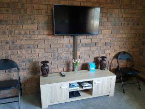 a tv on a brick wall with a table and two chairs at Inara Apartment Mudgee in Mudgee