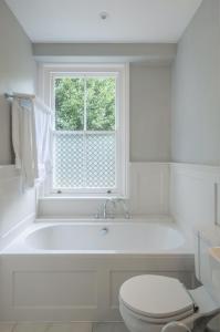 a white bathroom with a tub and a toilet and a window at The Nook at Henge Estate in Salisbury