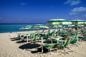 ein paar Stühle und Sonnenschirme am Strand in der Unterkunft Park Oasi Resort in Zambrone