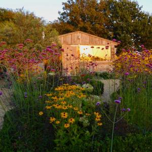 un jardín con flores frente a un cobertizo de madera en The Oaks Glamping - Rubie's Shepherds Hut en Colkirk