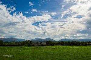 a green field with a cloudy sky and mountains at Red Robin Cottage in Gaerwen