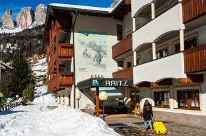 Una donna con i bagagli che passa davanti a un edificio nella neve di Garni Aritz a Campitello di Fassa