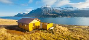 a small yellow house in front of a mountain at Langahlid Cottages & Hot Tubs in Seyðisfjörður