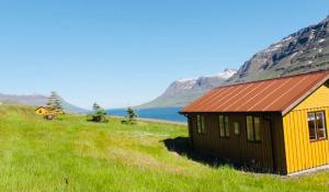 a yellow and black building in a field with a mountain at Langahlid Cottages & Hot Tubs in Seyðisfjörður