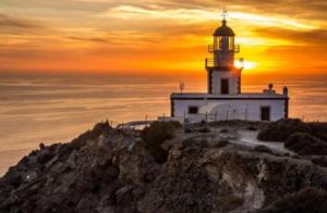 a lighthouse on top of a hill with the sunset at Golden Stone Santorini Suites in Akrotiri