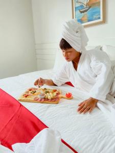 Eine Frau auf einem Bett mit einem Tablett Essen in der Unterkunft Pousada Capital das Águas in Maceió