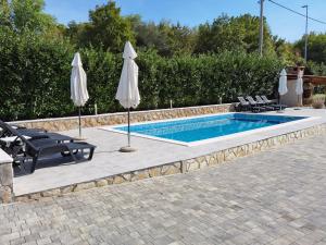 a swimming pool with two umbrellas and two chairs and a pool at Apartments Beciri in Sveti Vid-Miholjice